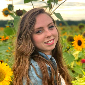 Picture of young woman with long brown hair and sunflowers in the background